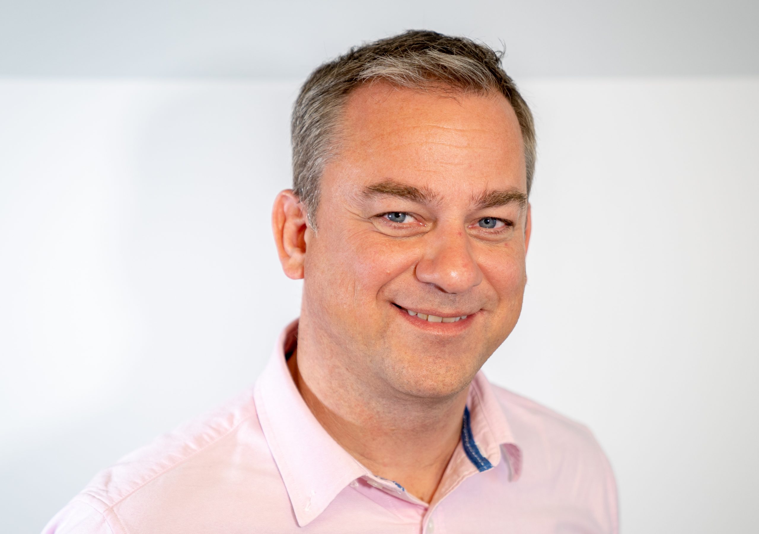 A man in a pink shirt smiles at the camera
