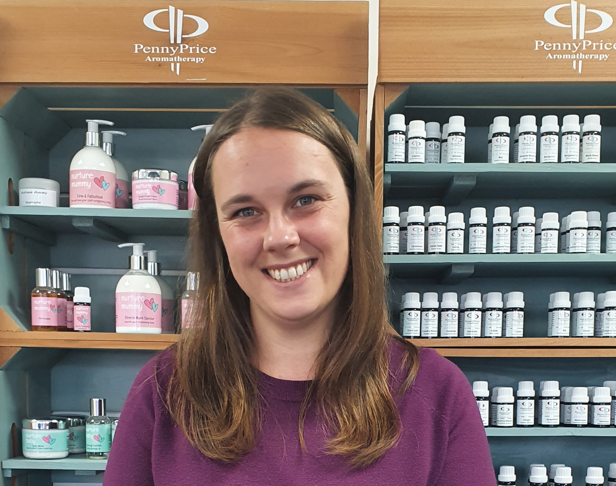 A woman with brown hair in a purple top stands in front of aromatherapy products