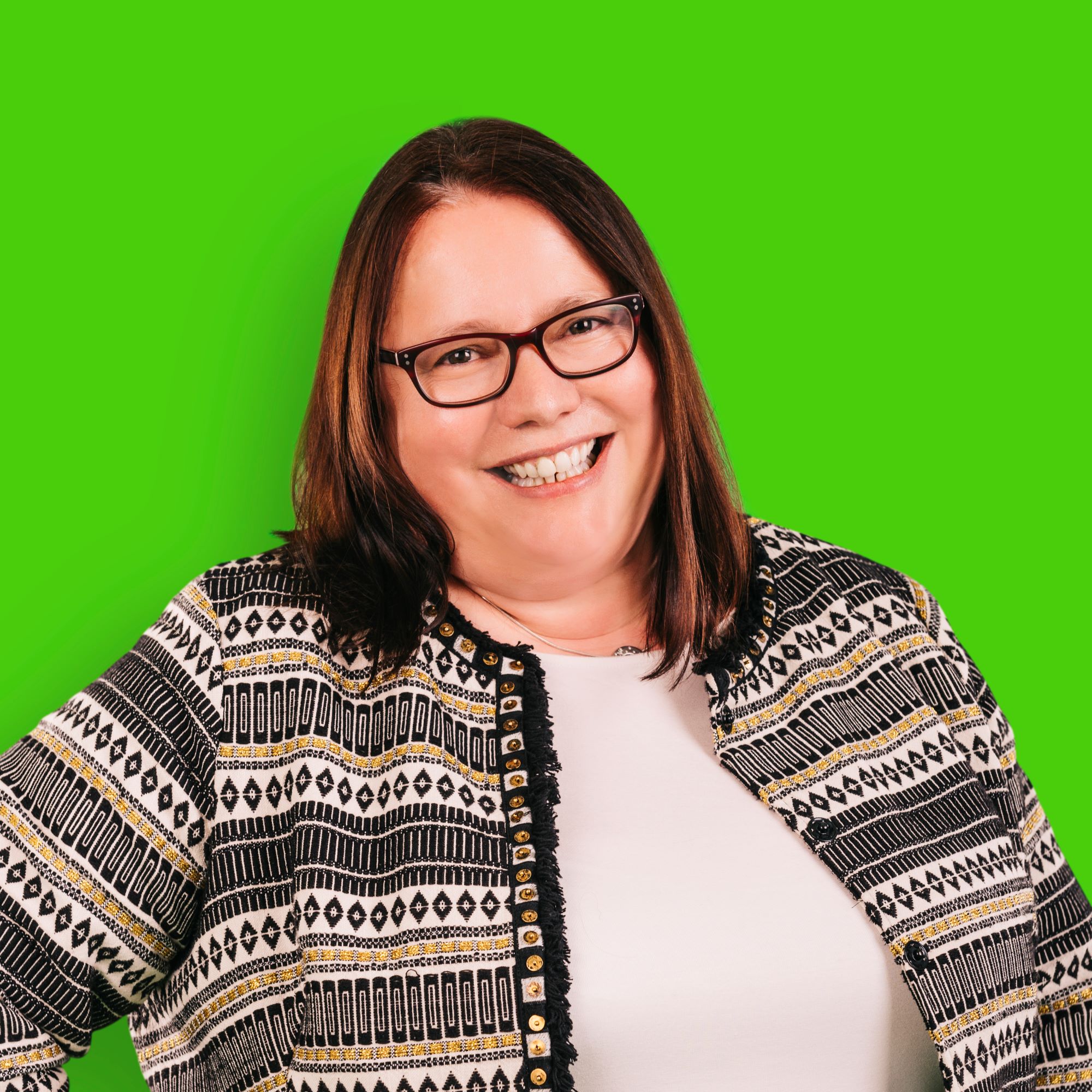 A woman with long brown hair and glasses is smiling at the camera.