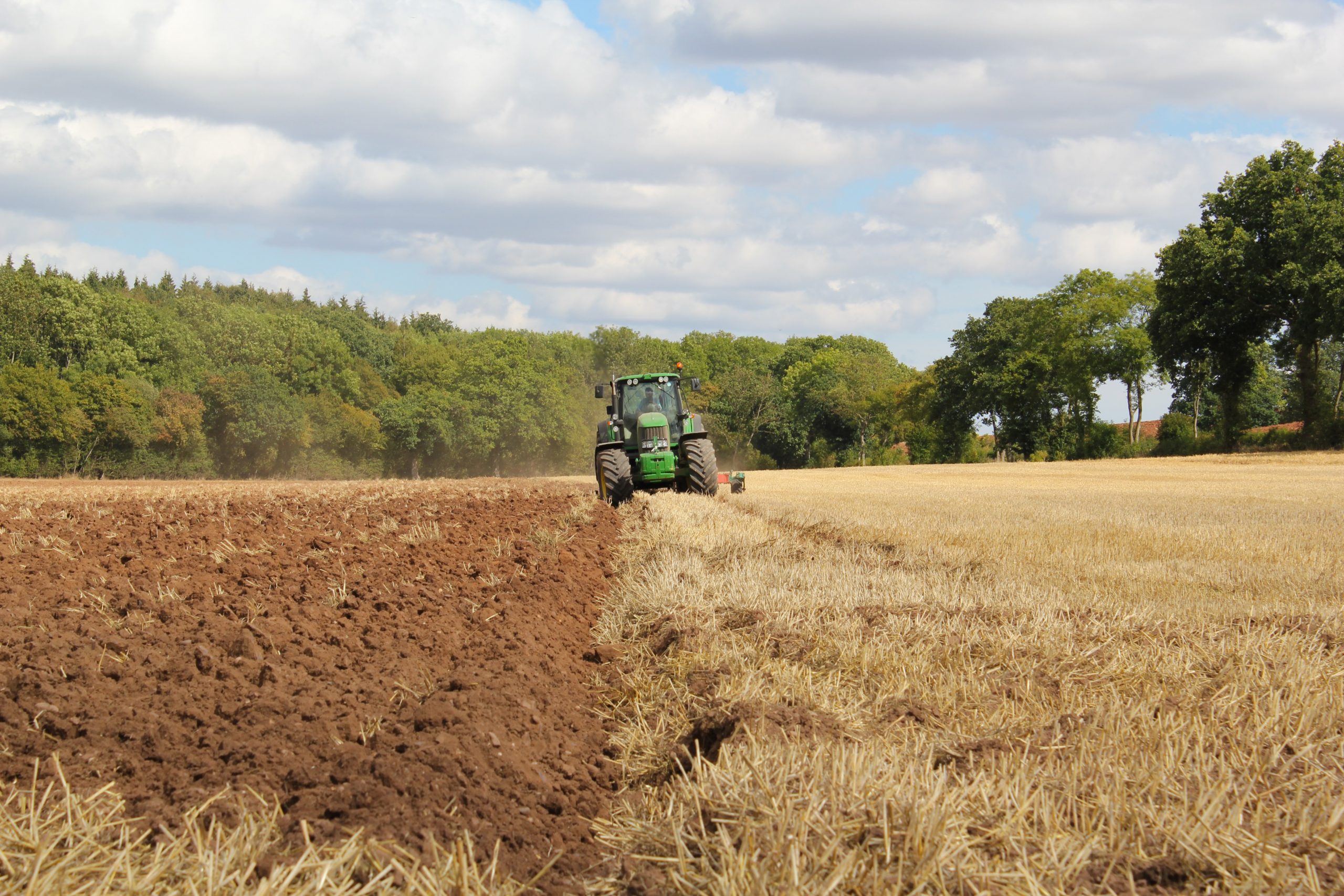 a green tractor ploughs a field