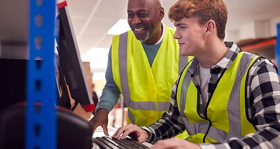 Two people in high viz jacket. One showing other something on a computer screen